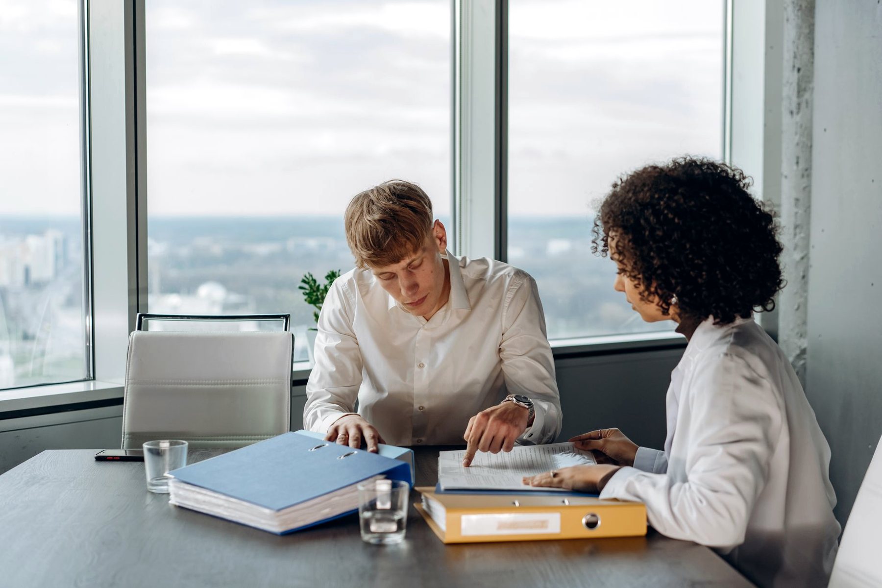 Deux collaborateurs relisent un dossier comptable, classeurs sur la table